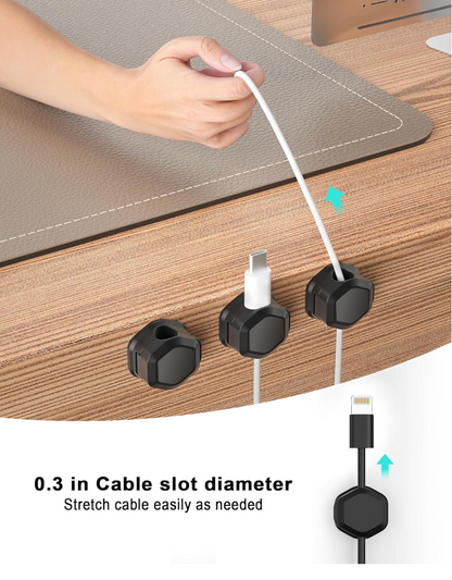 A close-up of a hand stretching a white cable through a black cable slot organizer on a wooden desk, with two additional slots shown holding cables. Text at the bottom reads '0.